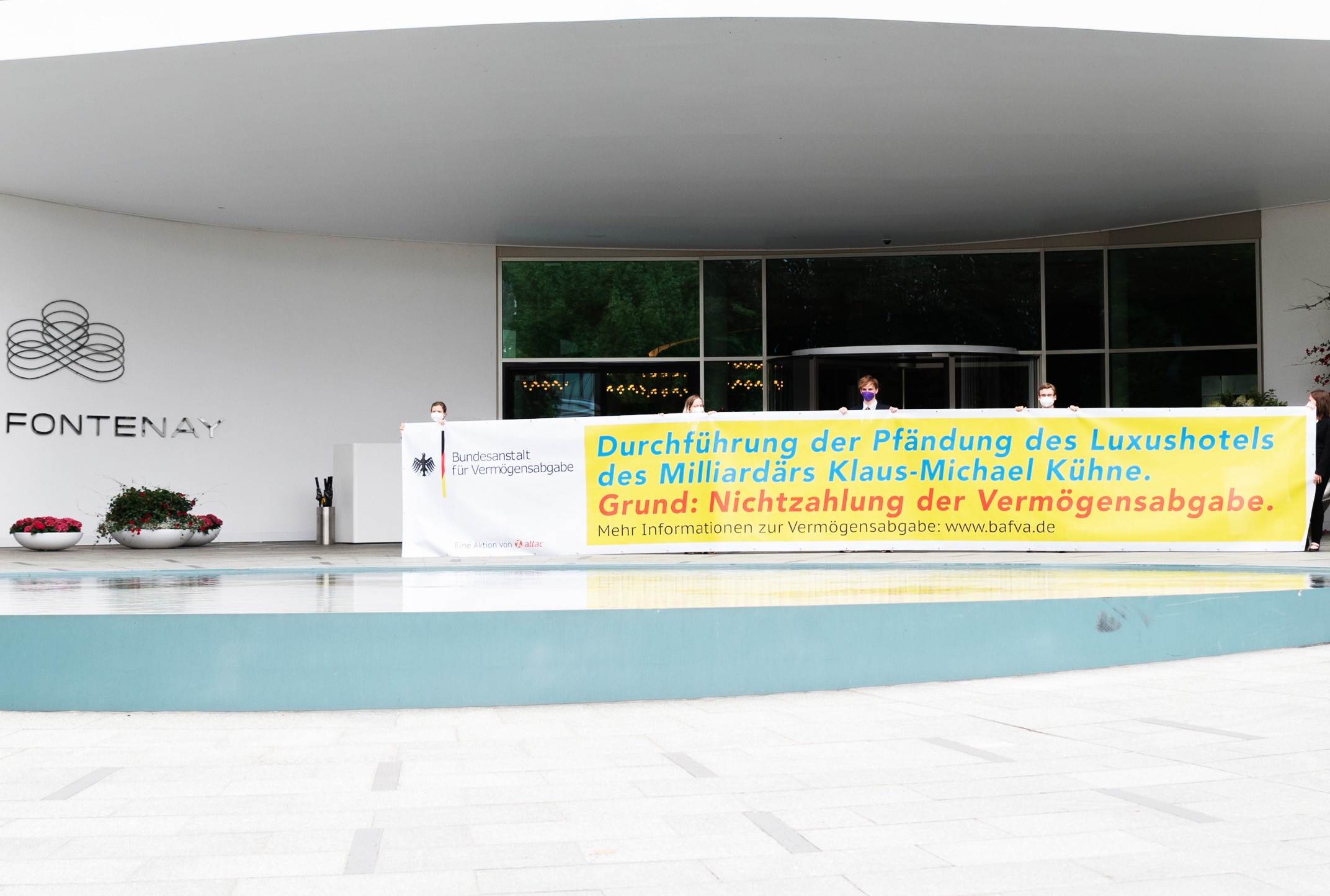Aktivist:innen halten ein Großes Banner vor dem Eingang des Luxushotels “The Fontenay”, in dem Sie im Namen der Bundesanstalt für Vermögensabgabe die Pfändung des Hotels verkünden