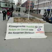 Ein Transparent ist auf dem Friedensplatz aufgespannt mit dem Slogan "Klimagerechte Mobilität für alle: Verkehr der Zukunft nicht den Konzernen überlassen"