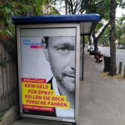 An einer Bushaltestelle hängt ein gefaktes FDP-Plakat mit Christian Lindner und dem Text "Kein Geld für ÖPNV? Sollen sie doch Porsche fahren."