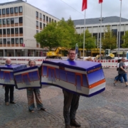 Auf dem Luisenplatz stehen drei Menschen in einer tragbaren Straßenbahn