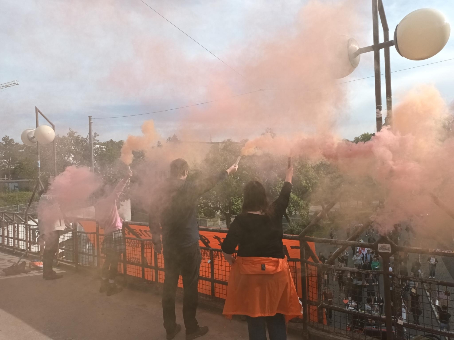 Auf einer Brücke stehen drei Menschen, die orangen Rauch hochhalten, vor ihnen hängt ein Transparent von der Brücke unter der die Demo entlaggeht