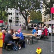 Leute sitzen auf Bierbänken und essen. Drumherum stehen verschiedene Pavillions.