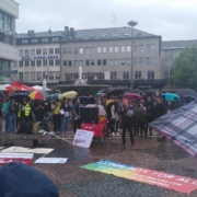 Menschen mit Regenschirmen stehen vesammelt um auf den Bodenliegende Transpis.