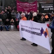 Auf dem Friedensplatz halten Aktivist*innen ein Banner mit der Aufschrift "Hand in Hand gegen den Rechtsruck – wir sind die Brandmauer