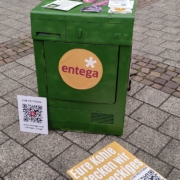 Grüne Waschmaschine mit entega Logo. An ihr ist ein QR-Code für eine Pedition gelehnt und darauf liegen verschiedene Materialien