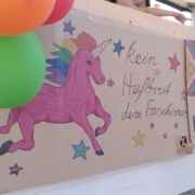 An einem Lautsprecherwagen hängt ein Schild mit einem rosa Einhorn und dem Spruch "Kein Hufbreit dem Faschismus" Daneben ein Schild mit dem Spruch "Queer sein ist keine Phase, Kapitalismus schon