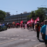 Demozug mit vielen roten Fahnen geht um die Ecke