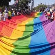 Sehr großes Regenbogenbanner, das von vielen Menschen getragen wird.